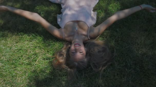 慢动作的上景从头长头发的女士躺在和举起双手背后的绿色草地在蕾丝阴凉的地方 — 图库视频影像