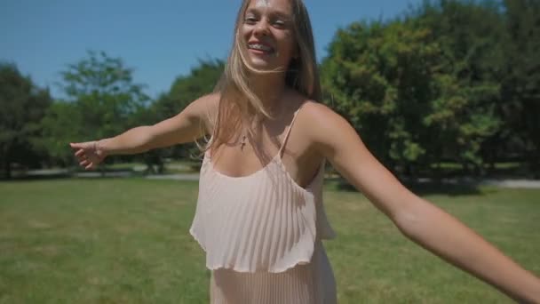 慢动作近视摄像头跟随金发女孩在绿色公园草坪上旋转和风浪长而松散流动的头发 — 图库视频影像