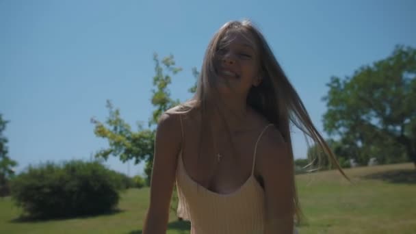 慢动作特写镜头金发女孩跳舞与长发在绿色公园草坪下的蓝天下随风飞舞 — 图库视频影像