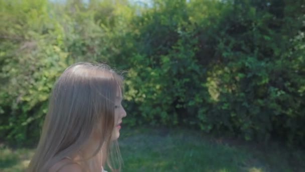 慢动作金发碧眼的长头发女孩在粉红色的太阳礼服坐在草地上打开笔记本电脑膝盖使惊讶的眼睛 — 图库视频影像