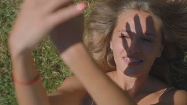 慢动作近高景观美丽的金发女孩躺在草地上 在阳光下用双手在脸上制作影子人物 — 图库视频影像
