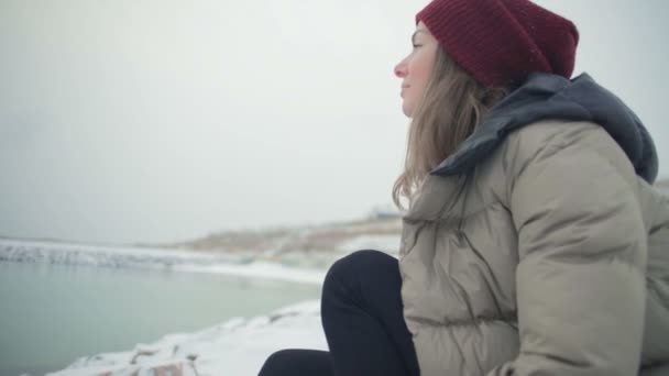 慢动作特写镜头梦幻般的女孩坐在岩石海滩上 在寒冷的冬日里带着鼓舞人心的微笑转身 — 图库视频影像