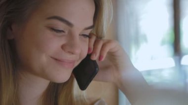 smartphone üzerinde konuşmak ve oturma kafede dizüstü bilgisayar ile gülümseyen güzel sarışın kadın