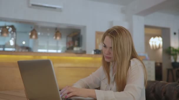 金发碧眼的女人坐在桌子和使用笔记本电脑上网 — 图库视频影像
