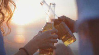 ağır çekim portre uzun saçlı kadın ve adam aşık şişe tıklatması ve güneş ışınları denizde akşam karşı öp