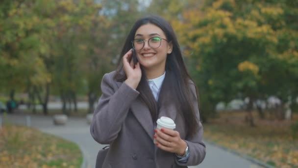 Улыбающаяся Брюнетка Очках Разговаривает Телефону Гуляя Осеннем Городском Парке — стоковое видео