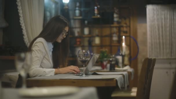 黑发妇女在眼镜喝红酒和与笔记本电脑在咖啡馆 — 图库视频影像