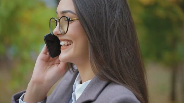 都市公園で携帯電話で話しているガラスのうれしそうなブルネット女性 — ストック動画