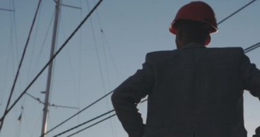 arka Görünümü Kapat adam kask siluet Yat Gemi direkleri ve masmavi gökyüzünde parlak güneş diski ışık karşı