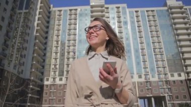 büyük binaya karşı akıllı telefon ile yürüyüş gözlük sarışın saçlı kadın 