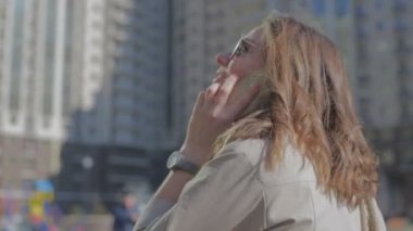 kadın güneşli bir günde binaya karşı telefonda konuşuyor
