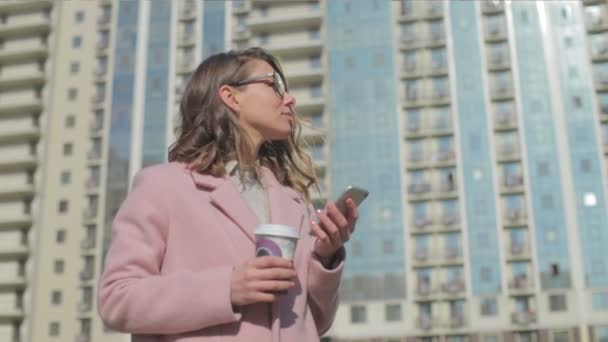 Žena Skleničkách Růžovým Kabátem Telefonem Kávě Stojí Proti Budově Slunném — Stock video