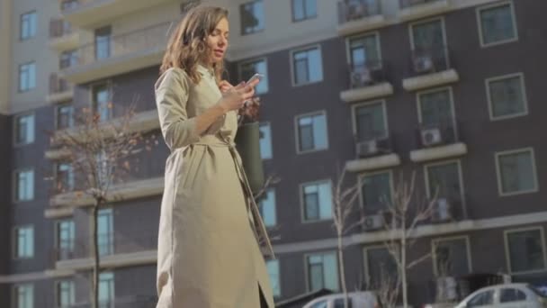 Vrouw Lichte Jas Wandelingen Bedrijf Smartphone Zoek Naar Woonhuis — Stockvideo