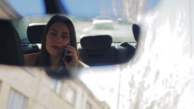 Uzun saçlı genç güzel esmer, akıllı telefondan konuşuyor ve dikiz aynasına yavaş çekimde yansıyor.