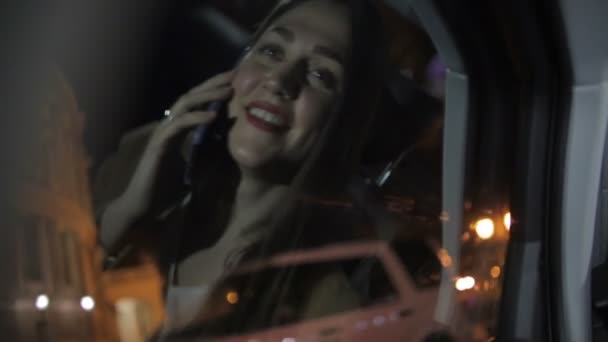 夜の運転車の窓に反映するスマートフォン上の赤い口紅の話を持つエキサイティングな長い髪の女性 — ストック動画