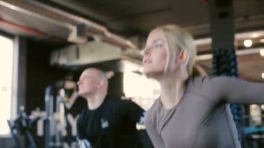 Modern spor salonunun düşük açılı çekimlerinde ağırlık sallayarak antrenman yapan profesyonel koçlar.