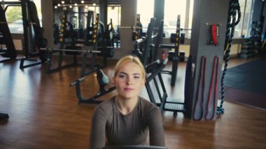 Açık renk saçlı güçlü kadın, kahverengi ahşap zemin ağır çekimde yeni büyük spor kulübünde kablolu yayında yer alıyor.