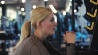 Kahverengi kazaklı ve beyaz tozluklu konsantre atletik bayan modern spor salonunda ağır çekimde çömelmiş.