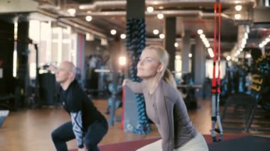 Modern spor salonunda siyah makinelerle el değiştiren kettlebell 'li aktif çiftler yavaş çekimde hareket ederler.