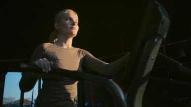 sporty girl practices cardio exercises on black velosimulator in sports club at sunset low angle shot slow motion