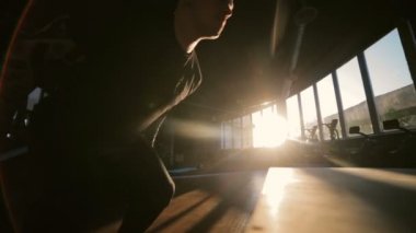 Kırmızı spor ayakkabılı kaslı adam ahşap desteğe atlıyor spor salonunda güneş tarafından aydınlatılıyor düşük açılı çekim yavaş çekim