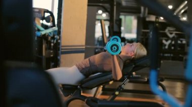 Eşofmanlı güçlü bir kız modern spor salonunda ağırlık kaldırma egzersizi yapıyor ve ağır çekimde ağır çekimde ağırlık kaldırıyor.