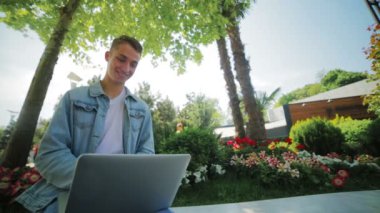 Mükemmel dişleri olan gülümseyen genç adam parkta internette sörf yapıyor.