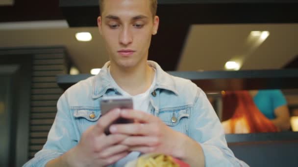 Концентрированный человек в джинсовой куртке держит и смотрит на телефон — стоковое видео