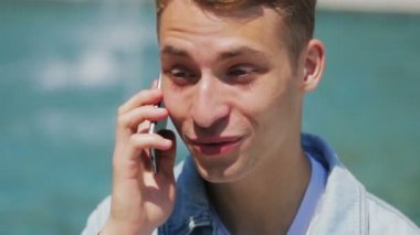 Mavi gözlü adam telefonu tutuyor ve arkadaşlarıyla konuşuyor.