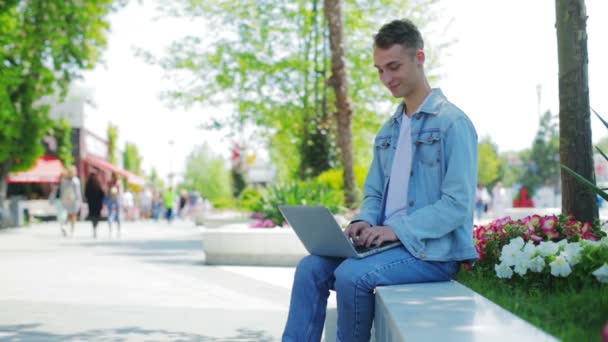 Pohledný muž v džínové bundě sedí na parapetu s notebookem — Stock video