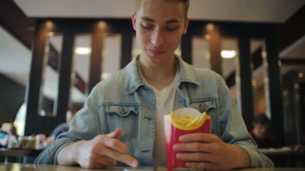 Guy in denim jacket eats french fries and swipes photos — Stock Video