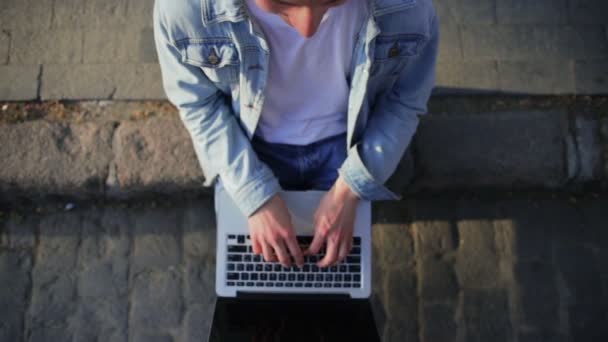 Pensando joven con el ordenador portátil se sienta en la frontera de la calle — Vídeo de stock