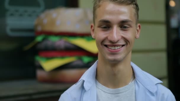 Guy smiles standing against blurry large hamburger statue Royalty Free Stock Footage