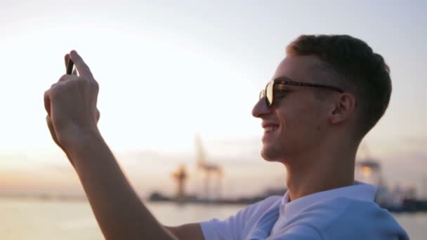 Вдячний хлопець у білій футболці та сонцезахисних окулярах робить фотографії — стокове відео