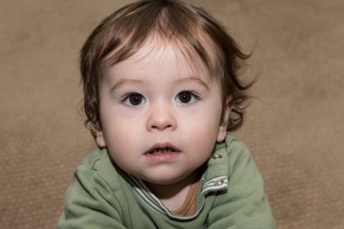 Bir buçuk yaşındaki çok yakışıklı bir çocuk bir evin halısında oynuyor.