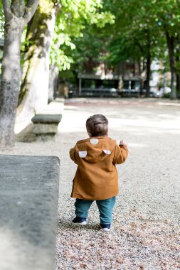 Bir buçuk yaşında bir bebek, gevşek bir taş zeminle parkta ilk adımlarını atıyor ve yürümeyi öğreniyor.