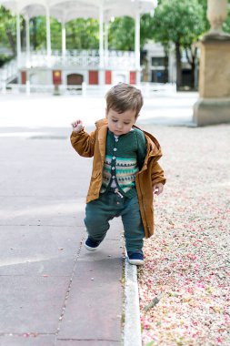 Bir buçuk yaşında bir bebek, gevşek bir taş zeminle parkta ilk adımlarını atıyor ve yürümeyi öğreniyor.