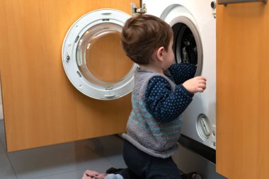 Çamaşırları yıkamak için çamaşır makinesini kurmaya yardım eden bir çocuk. Elbiseleri fıçıya koyuyor..