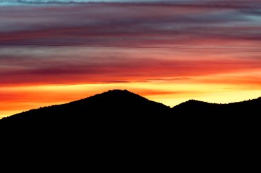 Bir dağın arkasında günbatımı, pembe, turuncu, mavi ve kırmızı gibi çok çarpıcı birkaç renk vardır..