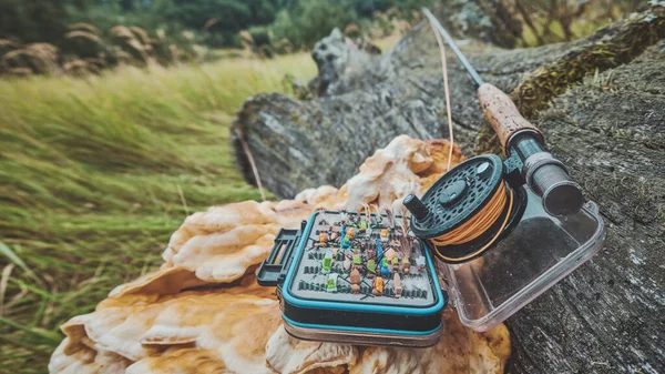 Fly fishing rod and box with flies on the background of a forest river.