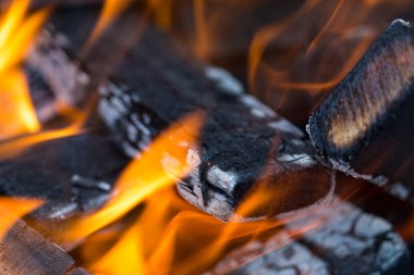 Alevler yakacak odunları yakar ve külleri dönüştürür. Yakın, sığ alan derinliği. Büyük bir fırında yak. Ateşin doğal dokusu. Alevler alev alev yanan odunları yakıyor..