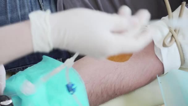 Givaren ger blod, sjuksköterska stick nålen i givare ven, pumpa blod. Blodgivning. Blodtransfusion, interiör, dagsljus — Stockvideo