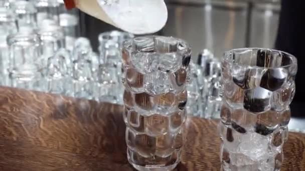 Лёд в коктейльных бокалах на стойке бара. Подготовка коктейля — стоковое видео