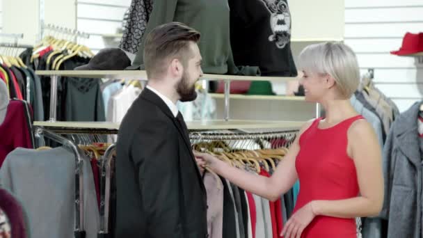 Het kiezen van nieuwe kleding. Gelukkig verleidelijke mooie lachende vrolijke volwassen paar kiezen nieuwe kleding in de winkel — Stockvideo