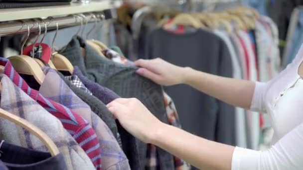 La mujer elige ropa en el centro comercial. Compras. Una mano de mujer quita la ropa de la percha de la tienda. Ropa colorida en perchas — Vídeos de Stock
