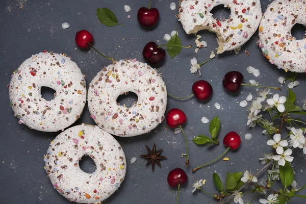 Algunos donuts con bayas de cereza en la mesa gris wiht flores top — Foto de Stock