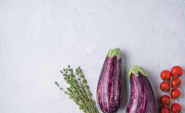 İki sulu patlıcan taze kekik ve kiraz domatesleri mavi bir masada yatıyor.