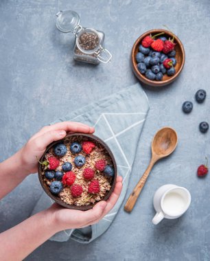   Eller Hindistan cevizi kasesini müsli ve böğürtlenli mavi arka planda tutar. Enerji ve vejetaryen kahvaltısı. Üst görünüm 