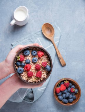   Eller hindistan cevizi kasesini enerji tanecikli ve böğürtlenli mavi arka planda tutar. Enerji ve vejetaryen kahvaltısı. Üst görünüm 