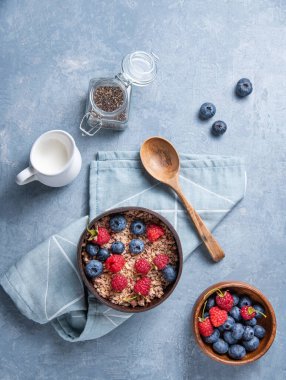 Ahududulu, yaban mersinli, chia tohumlu ve sütlü enerji müsli mavi arka planda hindistan cevizi kasesine. Üst görünüm 